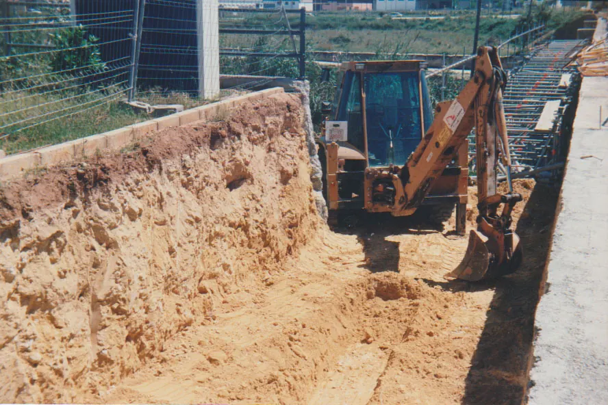 Retroexcavadora excavando una zanja junto a un muro (Excavaciones Subiela, Benaguasil)